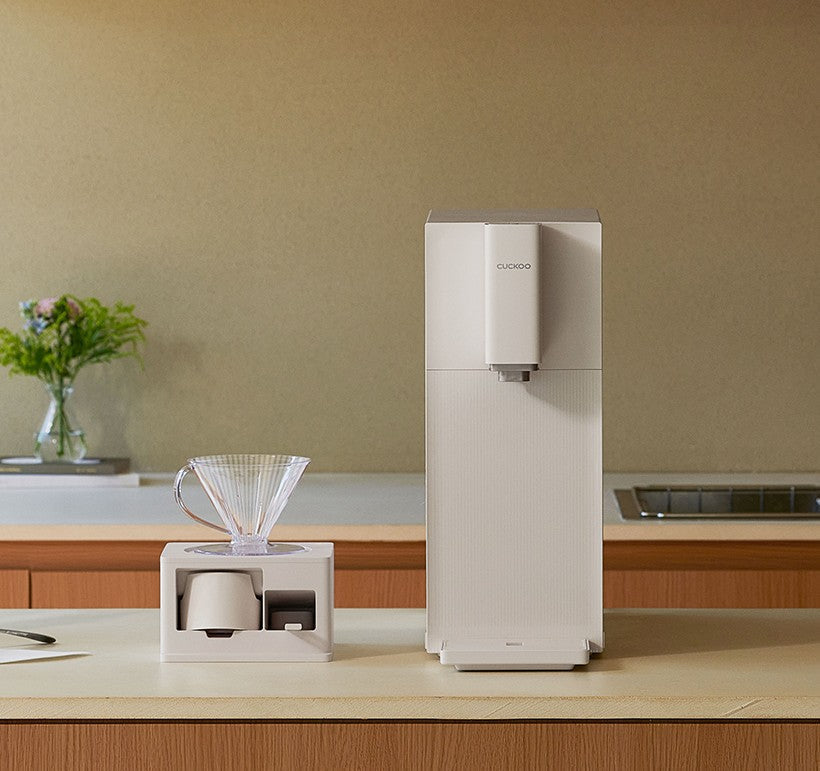 Cuckoo water purifier on a kitchen counter next to a white drip coffee station with a clear glass pour-over cone.